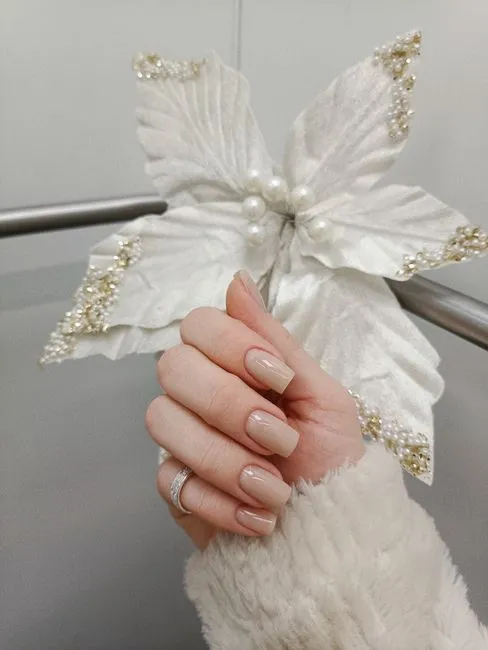 Neutral gel nails held against a white flower