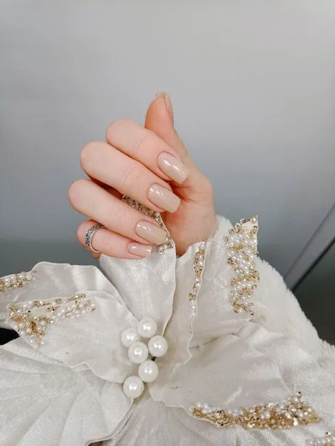 Nude nails finished for an occasion, against ivory fabric