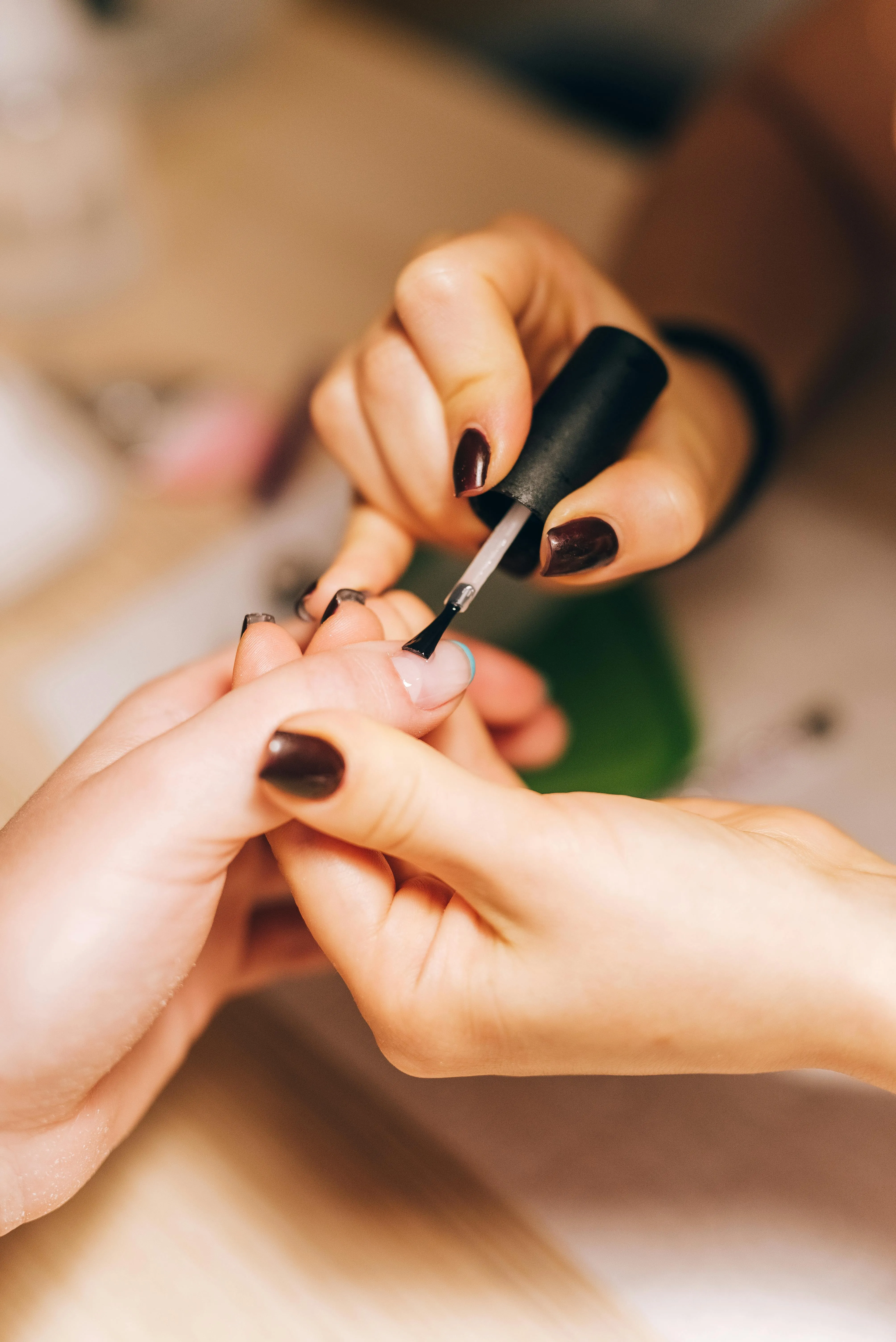 Kitty painting a deep berry polish onto a client's nails in warm studio light